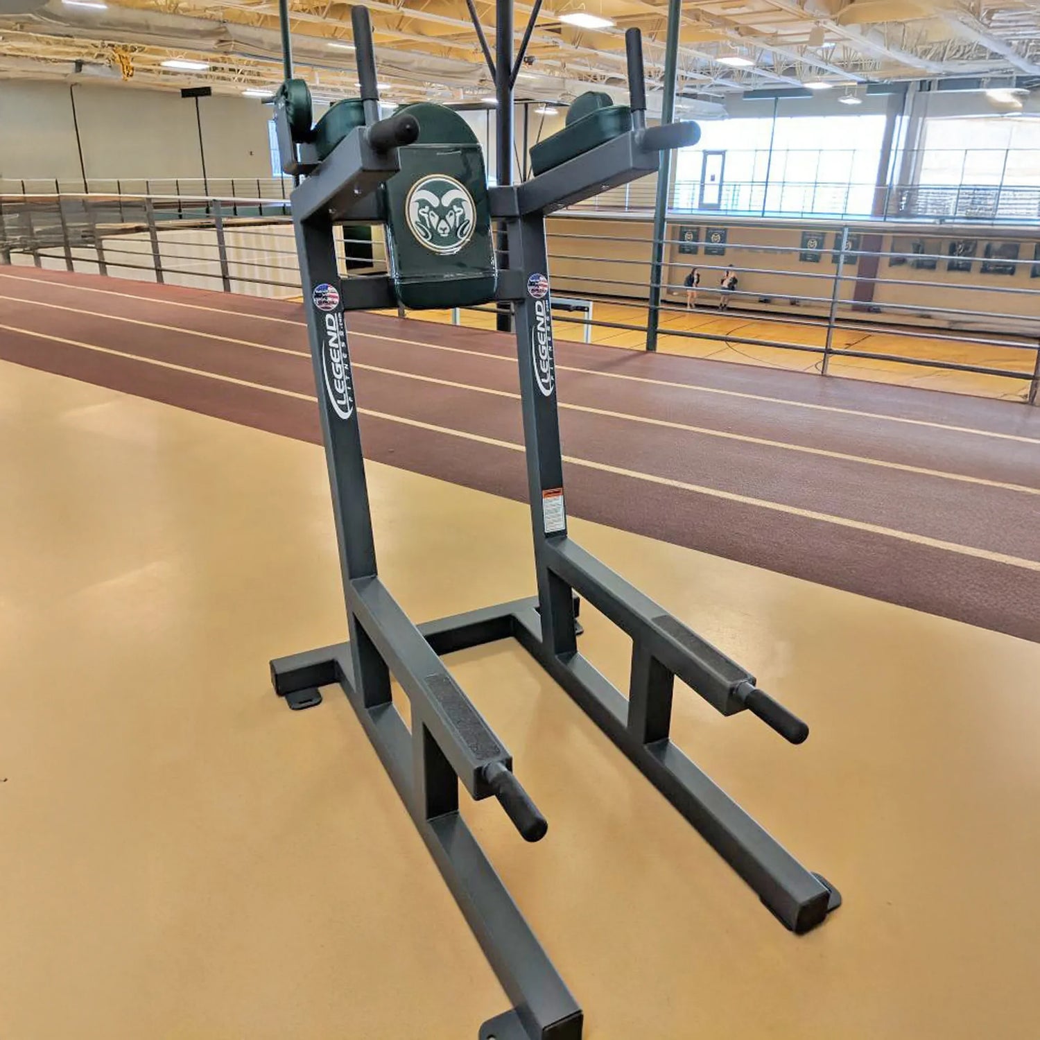 A gray metal crunch chair with green upholstery with a 'CSU Rams' logo on it in a fitness center setting