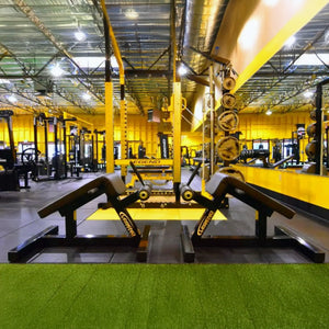 A gym with black and yellow fitness equipment with green artificial turf in the foreground