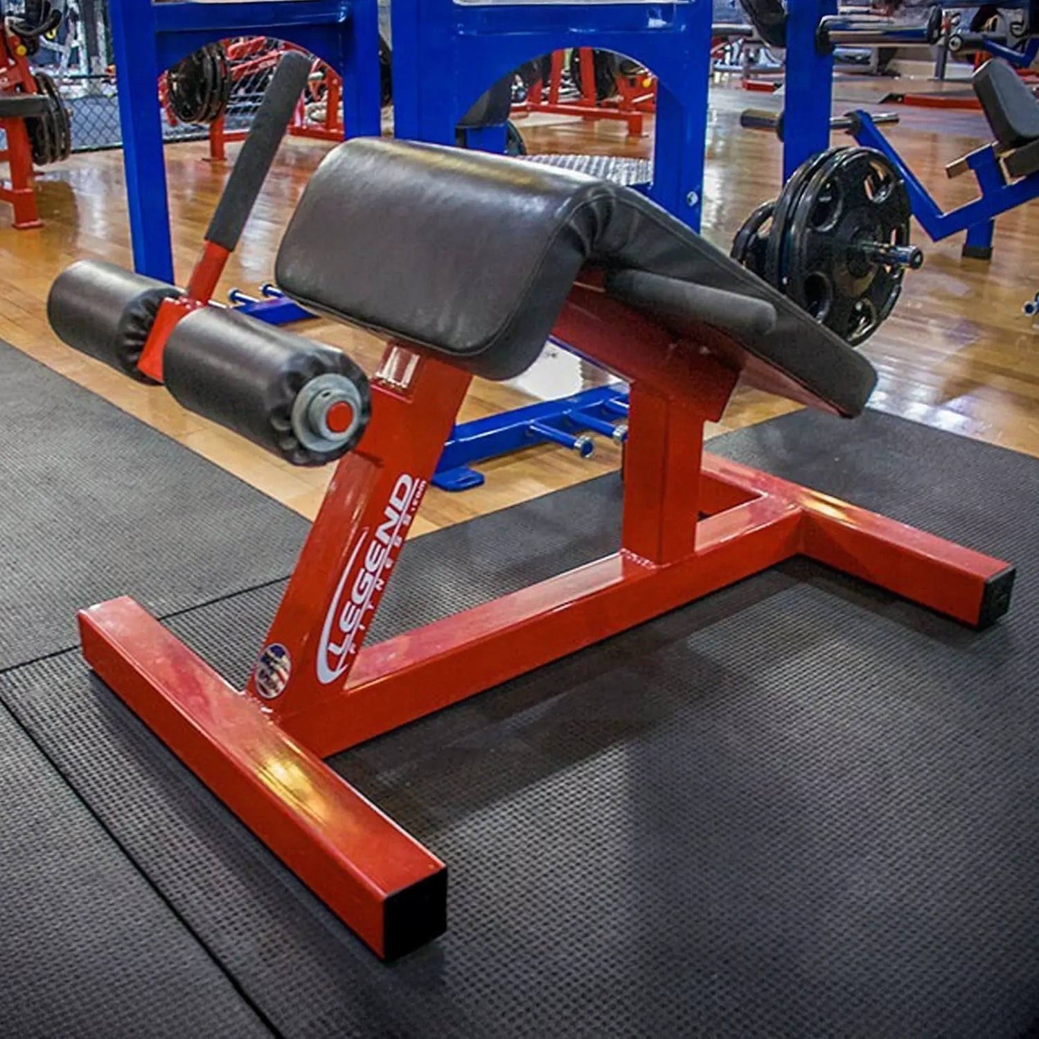 A red and black angled fitness sit-up bench in a gym setting