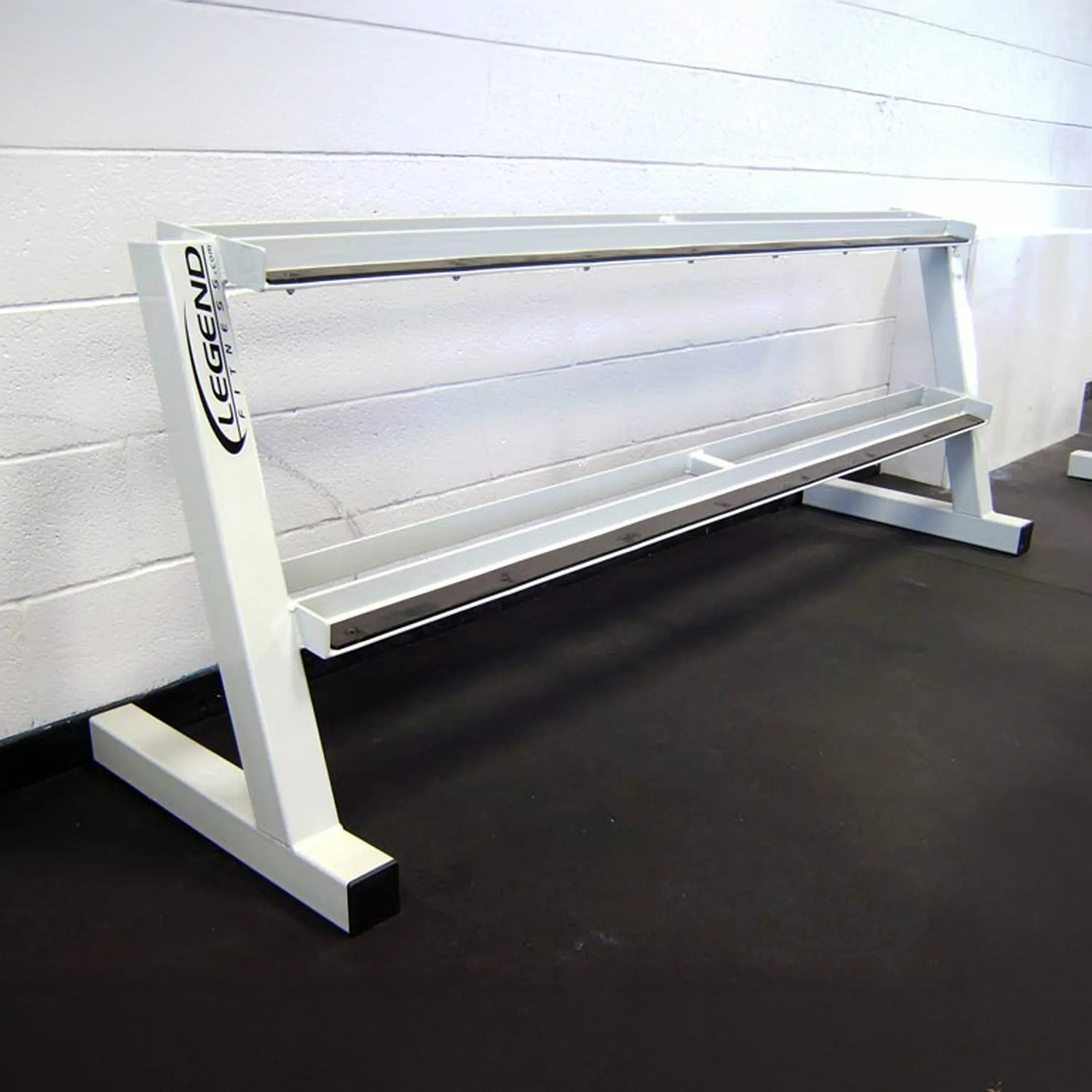 A white empty dumbbell rack against a white wall on a black rubber floor