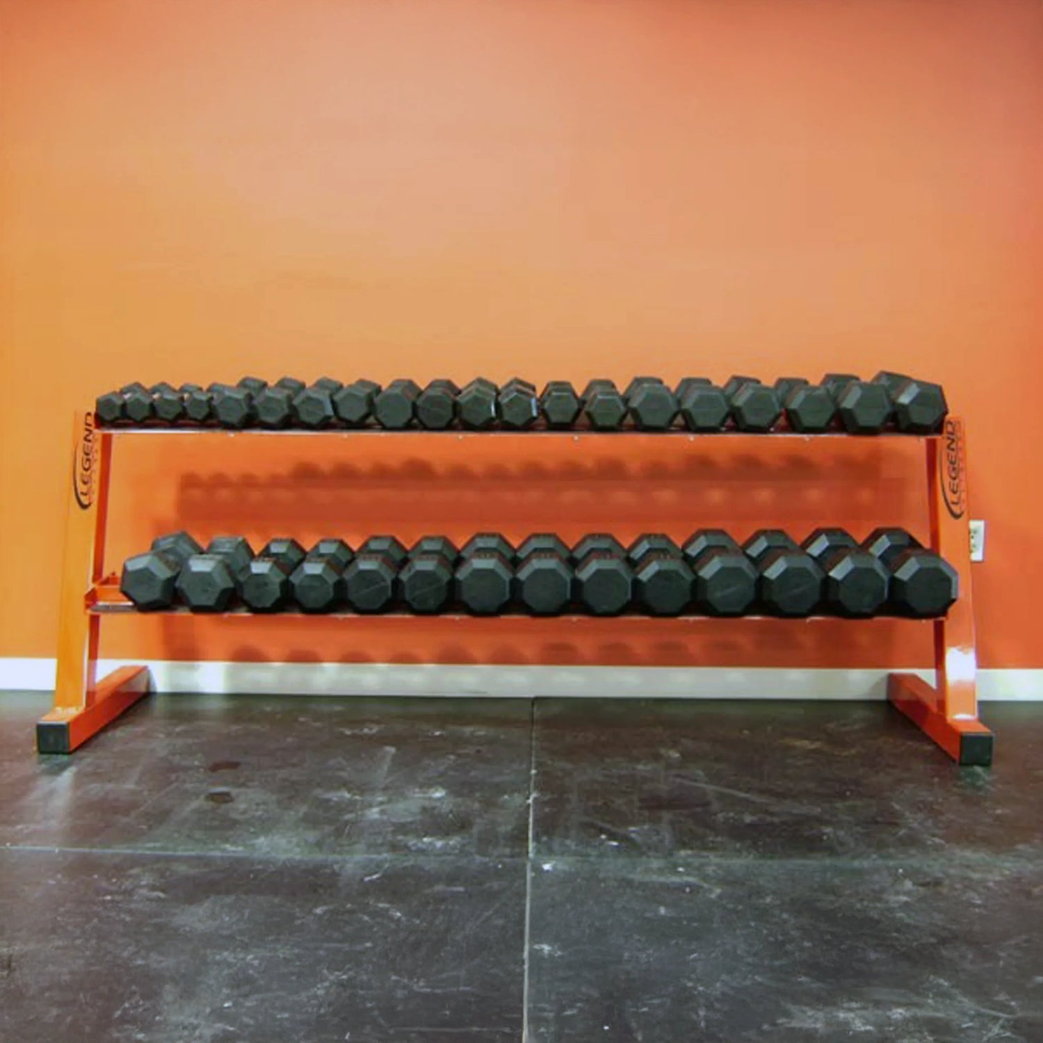 Row of black dumbbells on an orange rack against an orange wall.
