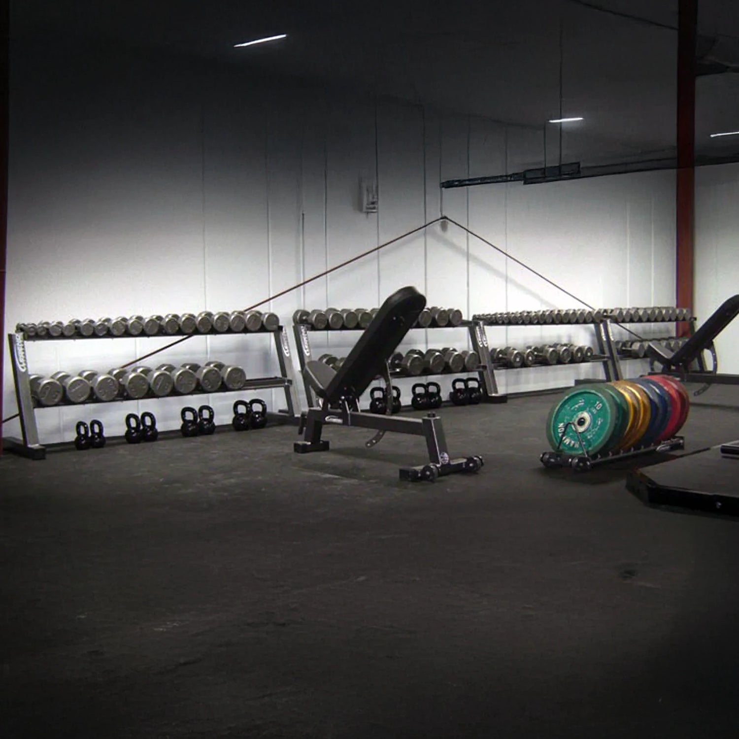 Gym interior with weight racks and dumbbells on a concrete floor.