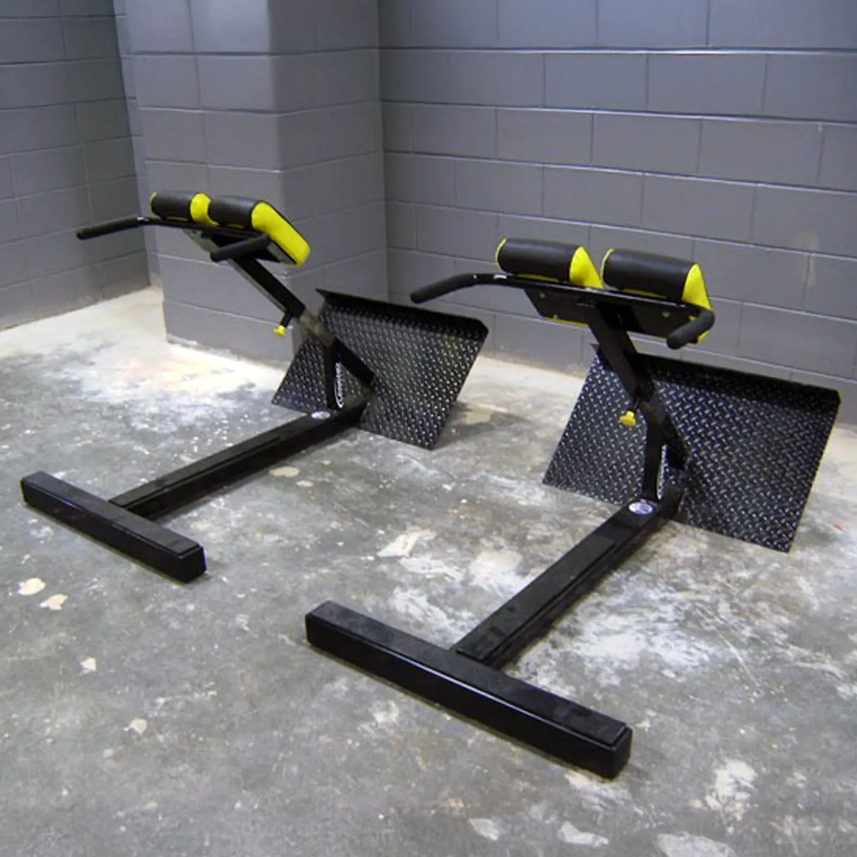 Two black and yellow hyperextension gym machines on a concrete floor