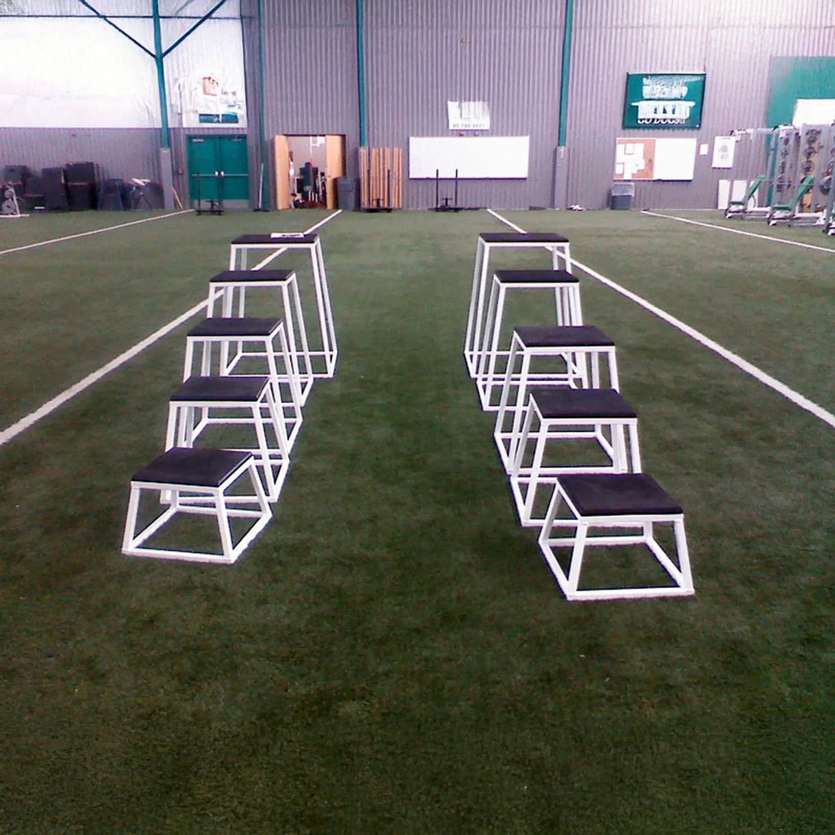 Set of white and black training steps on a grassy field with a building in the background.