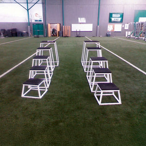Set of white and black training steps on a grassy field with a building in the background.