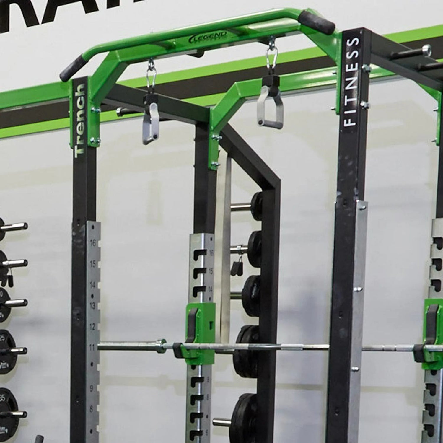 Green and black fitness power rack with weights in a gym setting