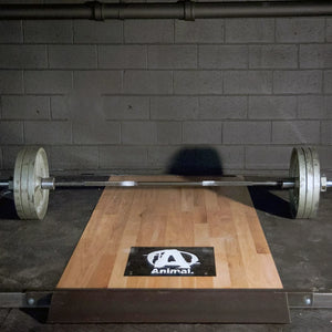 Wooden weightlifting platform with a barbell and 'Animal' logo on it on a dark brick wall background