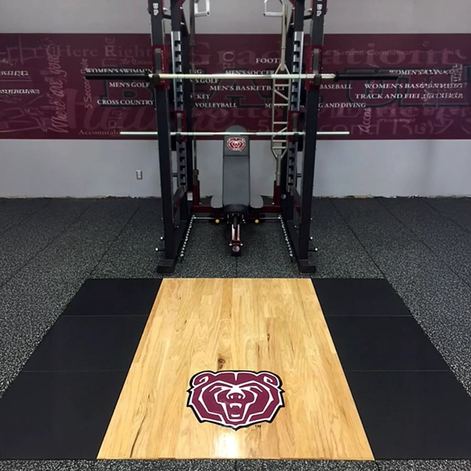 Wooden mat with a bear logo on a black and gray floor in a gym setting.
