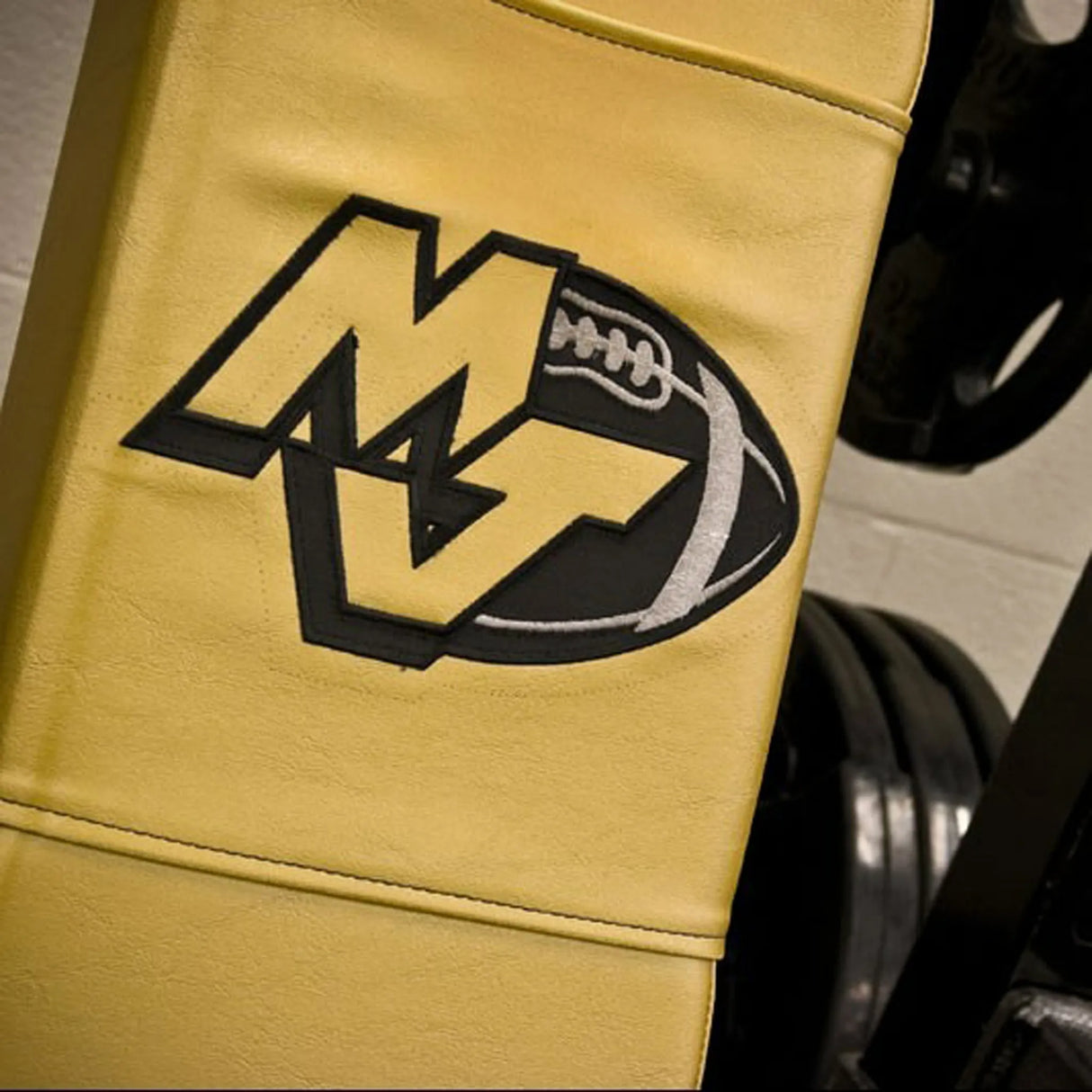A gold gym bench with 'MJ' and a football image embroidered on the pad