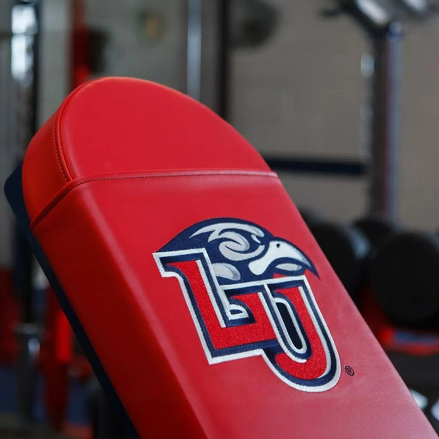 Red weight bench with a blue, red, and white 'LU' logo on it in a gym setting