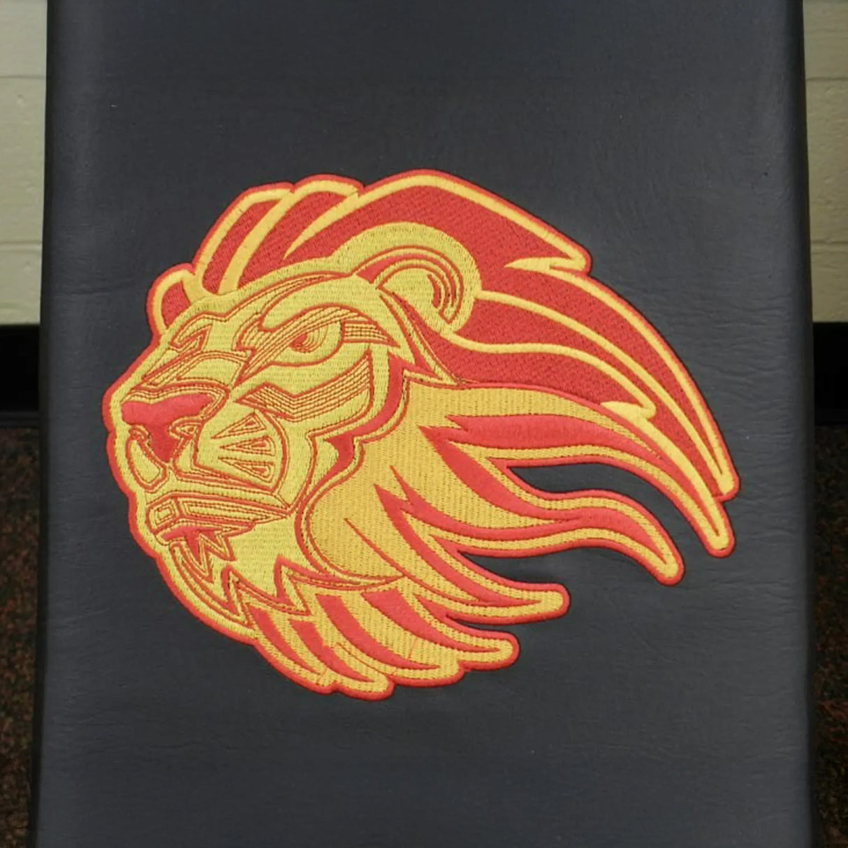 Embroidered lion logo on a black upholstered gym bench