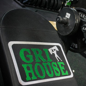 Grit House logo embroidered on a black bench pad with gym equipment in the background