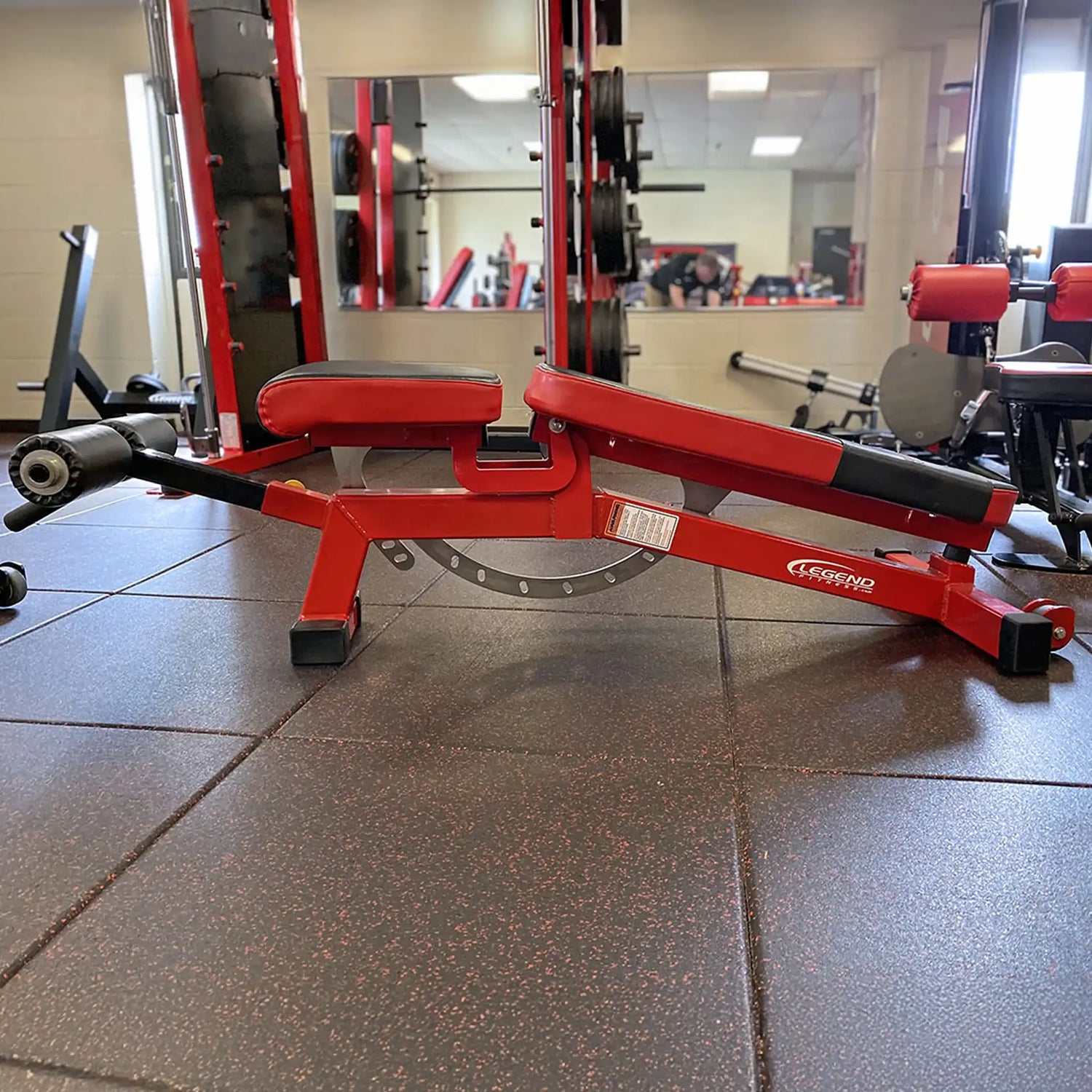Red weight bench in a gym setting with mirrors reflecting other equipment.
