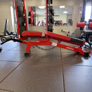 Red weight bench in a gym setting with mirrors reflecting other equipment.