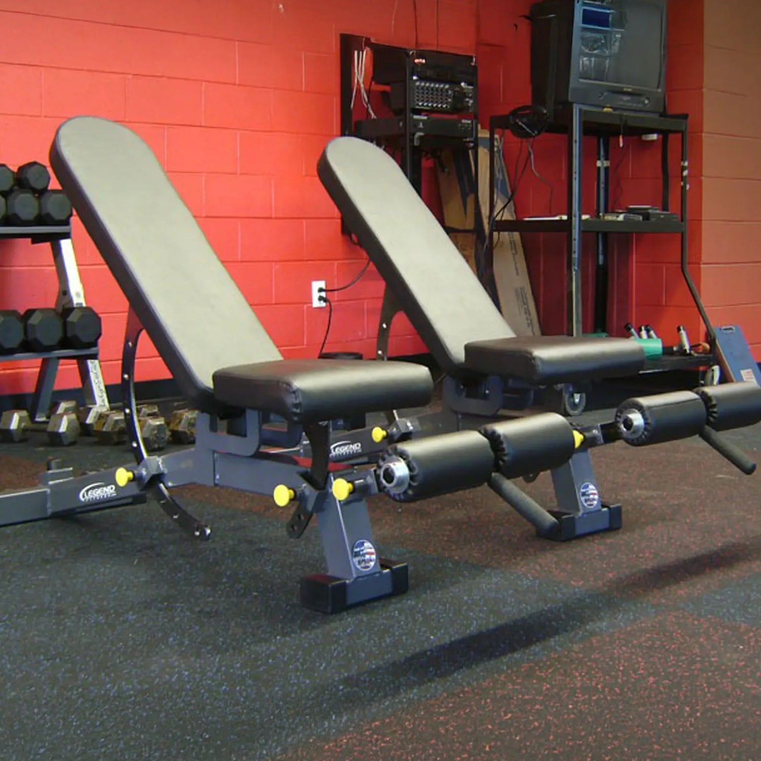 Two adjustable weight benches in a gym setting with red walls and equipment in the background.