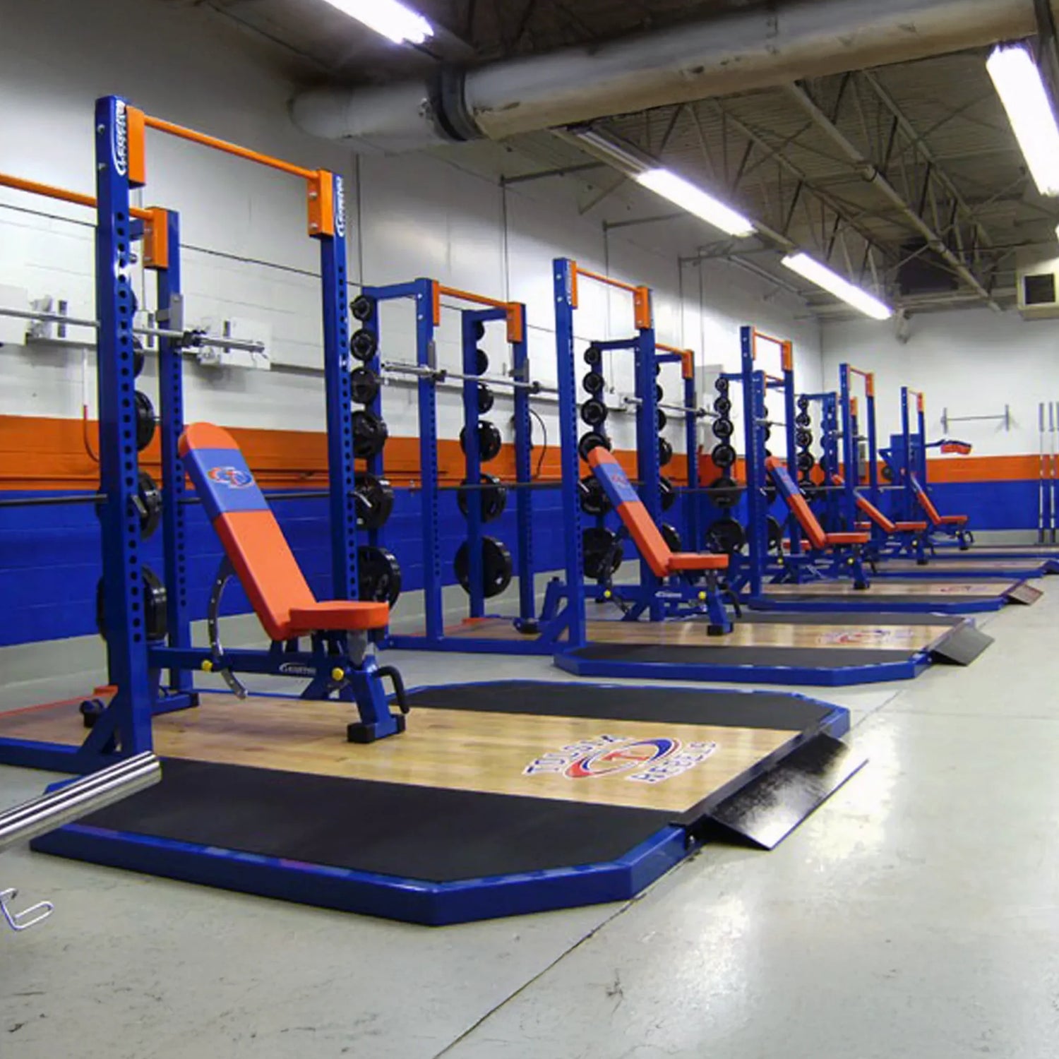Gym with blue weight racks and orange benches in a well-lit indoor facility.