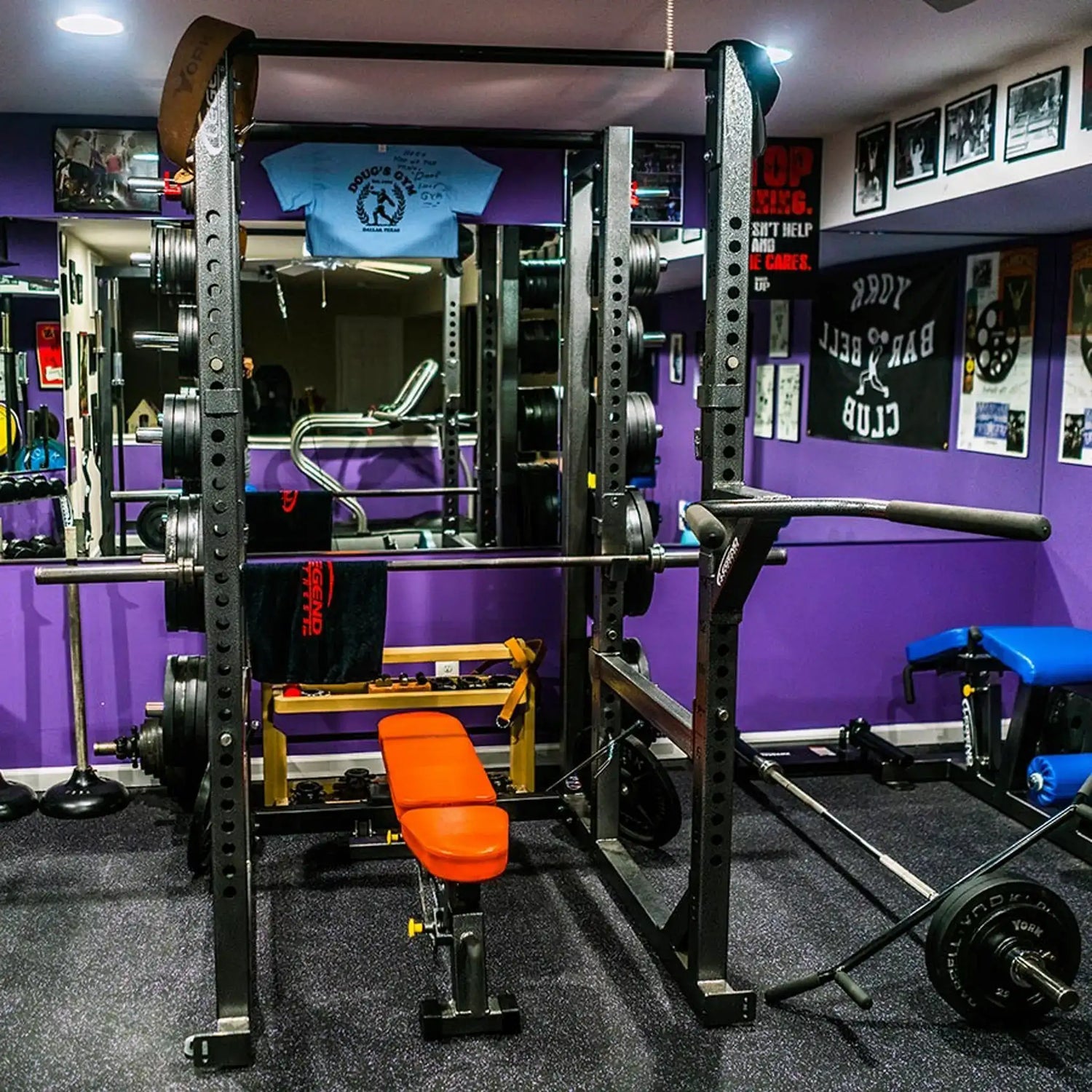 Gym interior with weightlifting equipment, including a squat rack and barbell, against a purple wall.