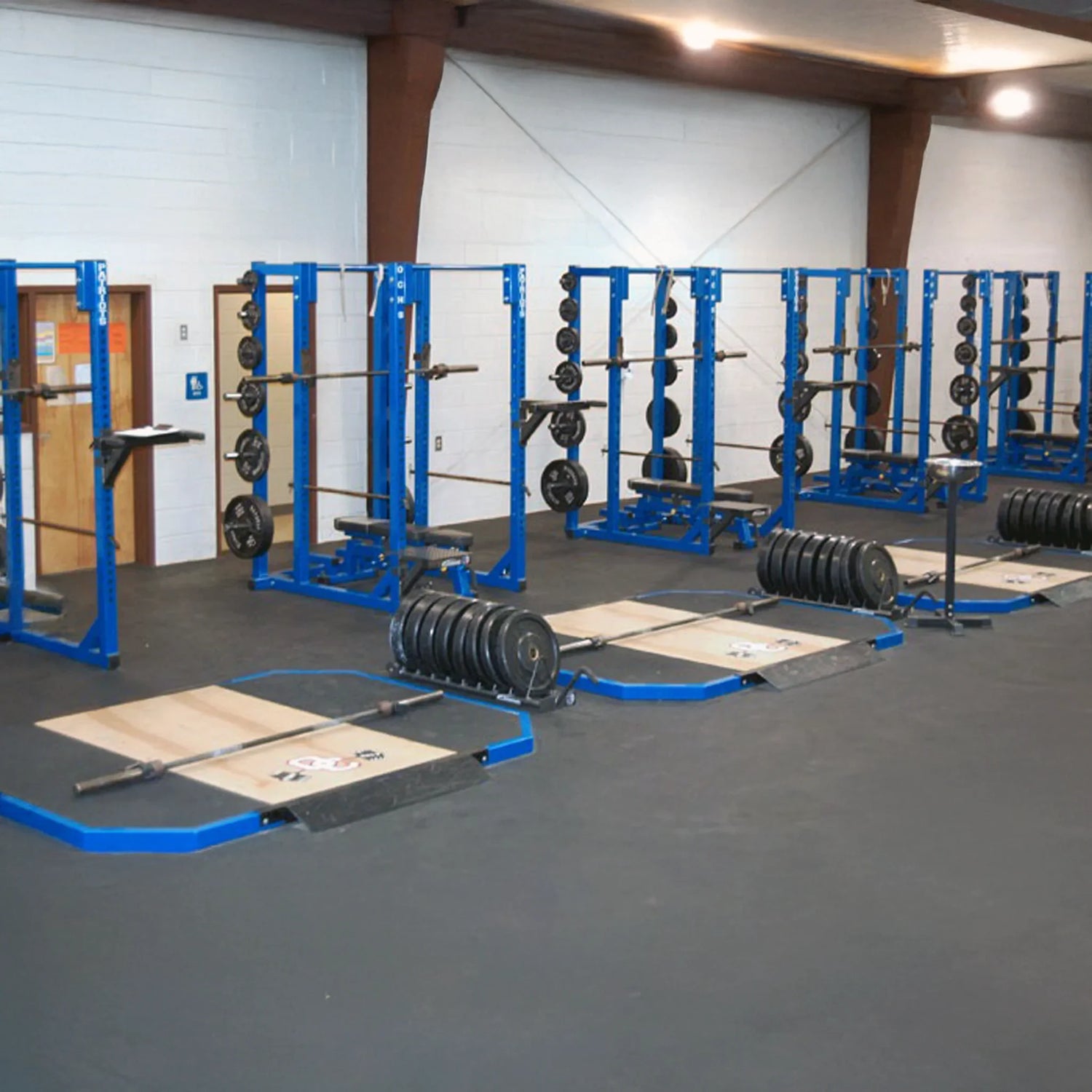 Gym interior with blue weightlifting racks and weights on a gray floor.