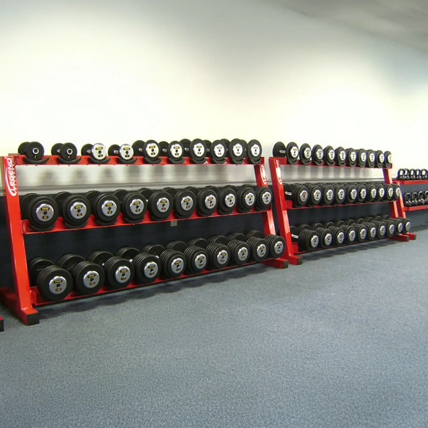 Row of red dumbbell racks with weights on a gray floor.
