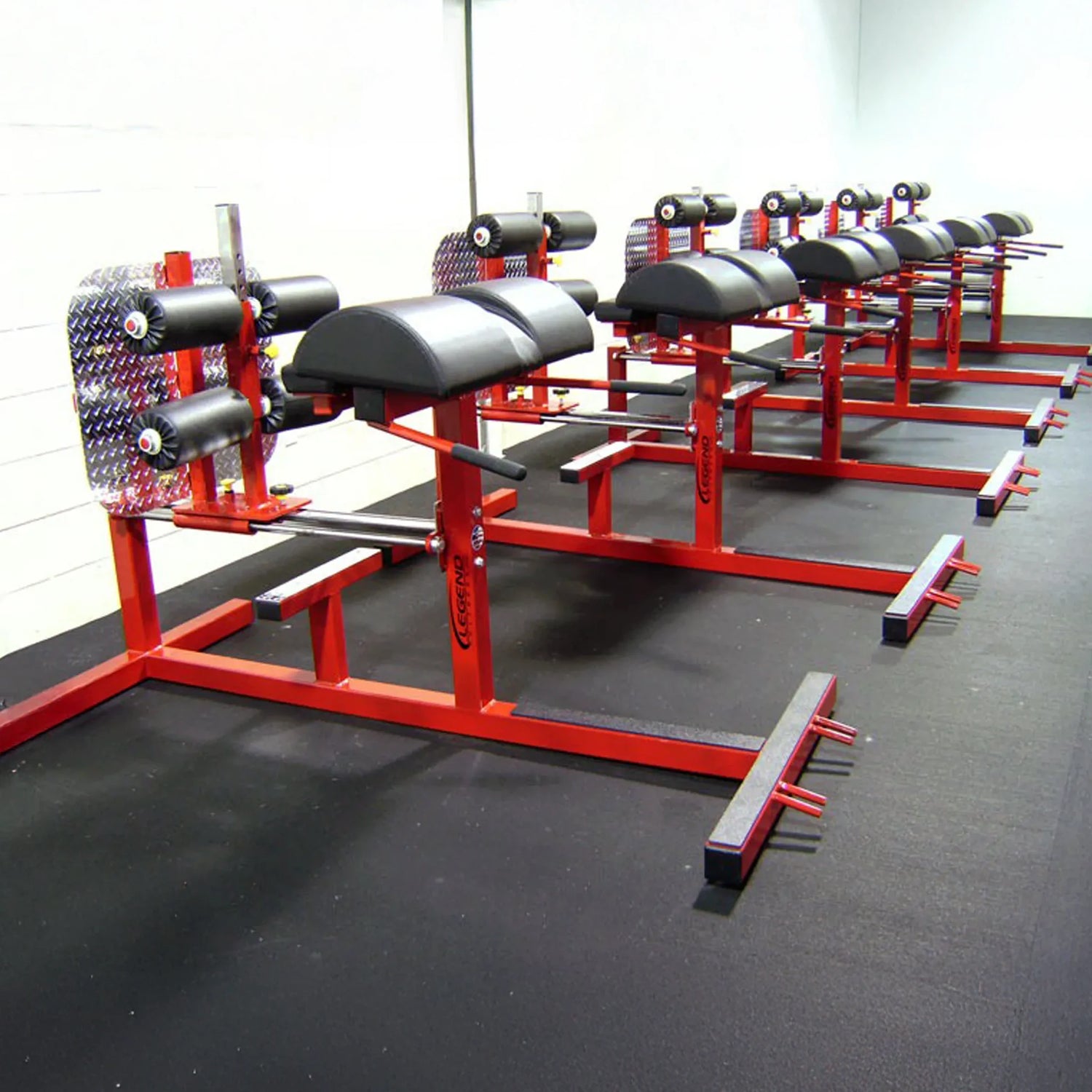A row of red and black glute ham developer fitness machines in a gym setting