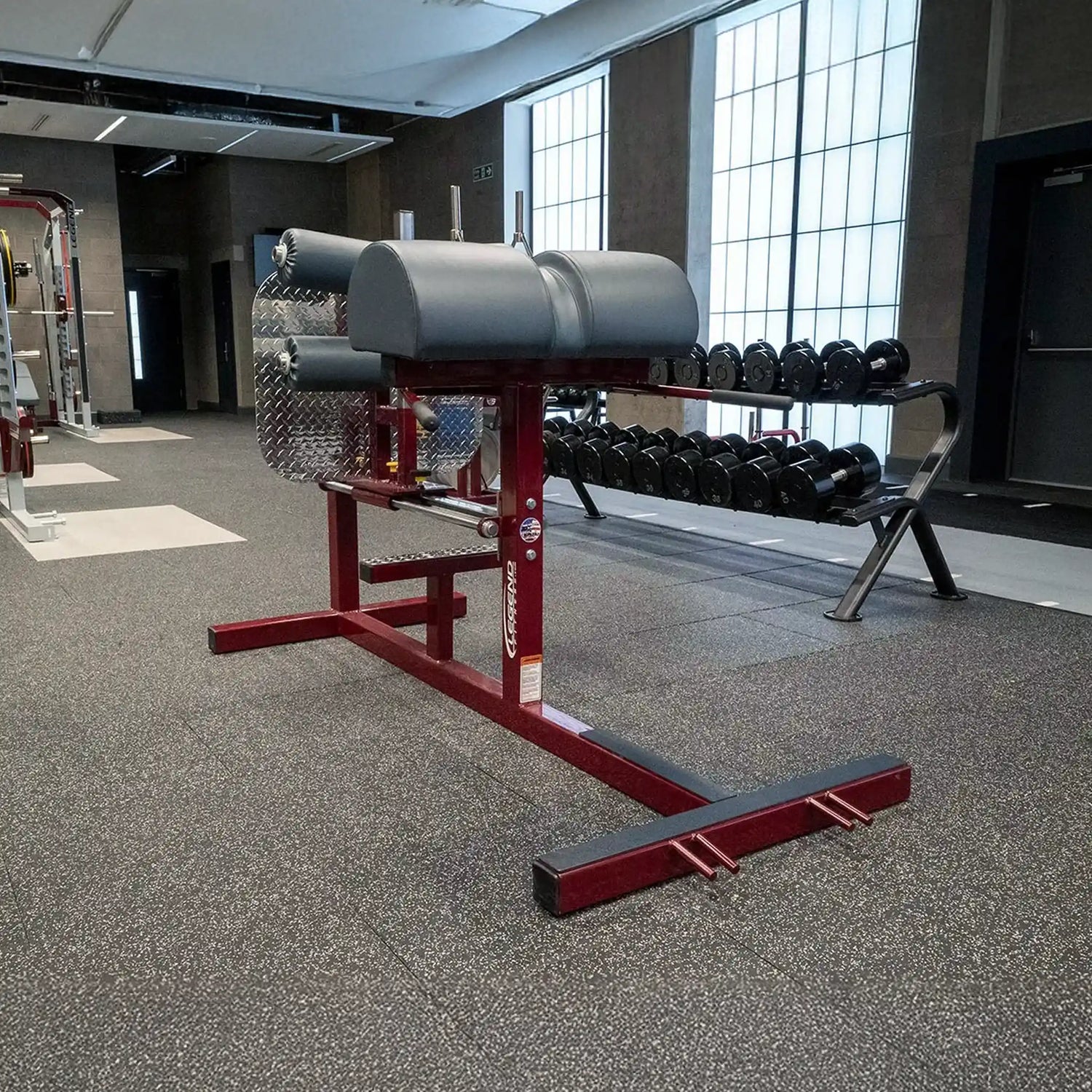 A red glute ham developer fitness machine with black pads in a gym setting