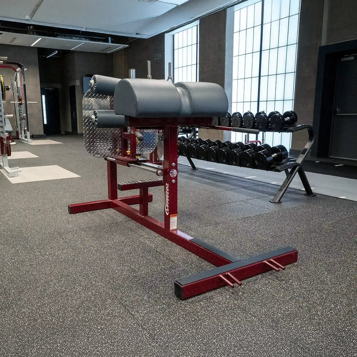 A red glute ham developer fitness machine with black pads in a gym setting