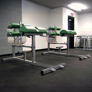 Silver glute ham developer fitness machines with green pads in a gym setting