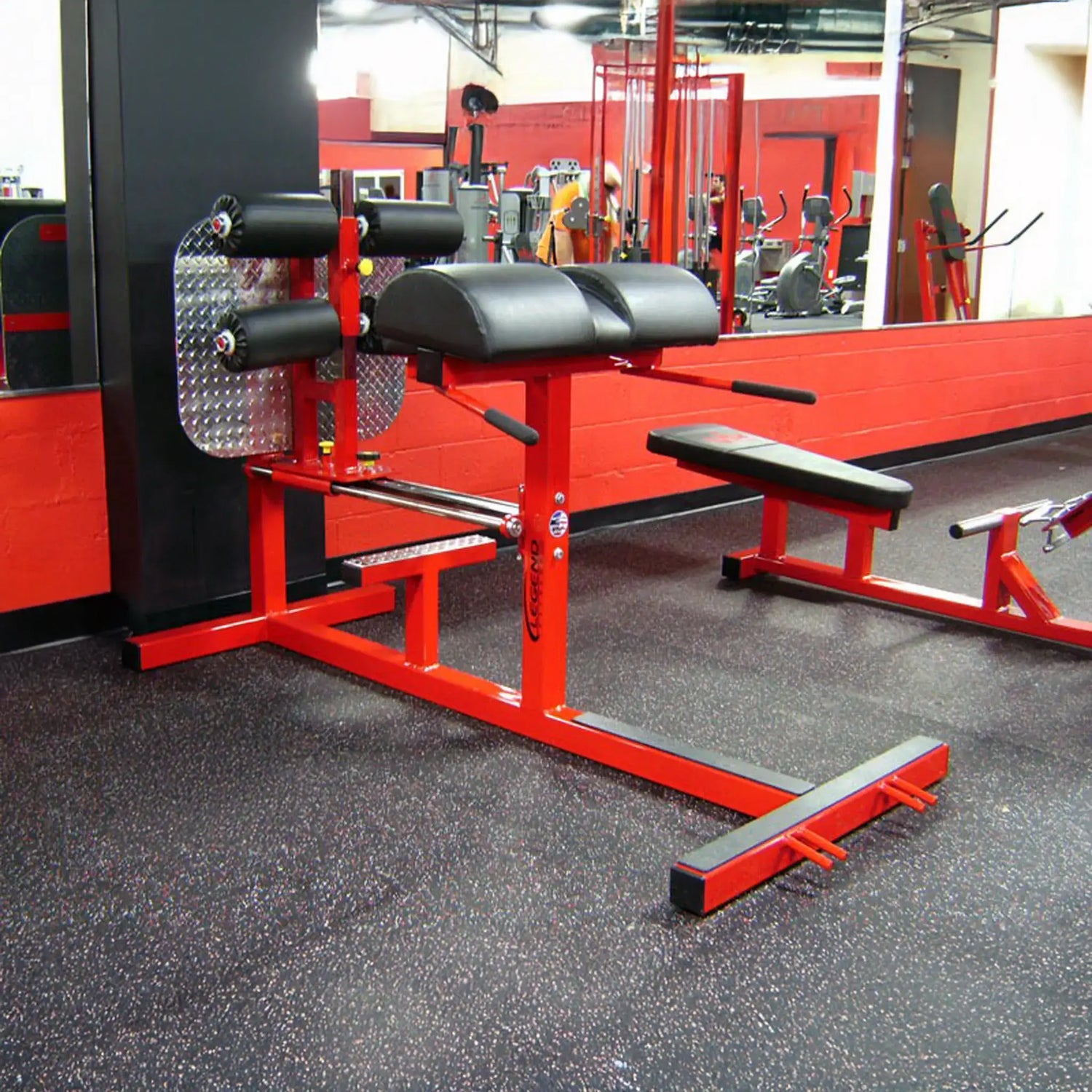 A red glute ham developer fitness machine with black pads in a gym setting