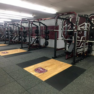Gym interior with weightlifting equipment and branded mats on the floor.