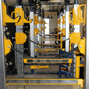 A look down the inside of multiple squat racks in a row showing yellow barbell hooks, safety straps, and safety arms