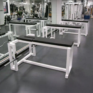 A row of three black and white prone row weightlifting benches in a gym setting