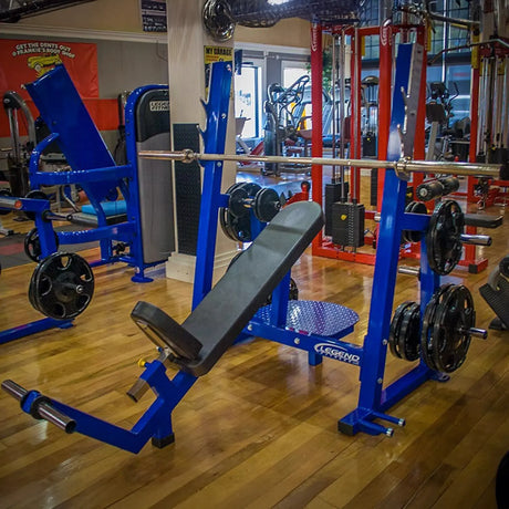 A blue and black incline Olympic bench press in a gym setting.