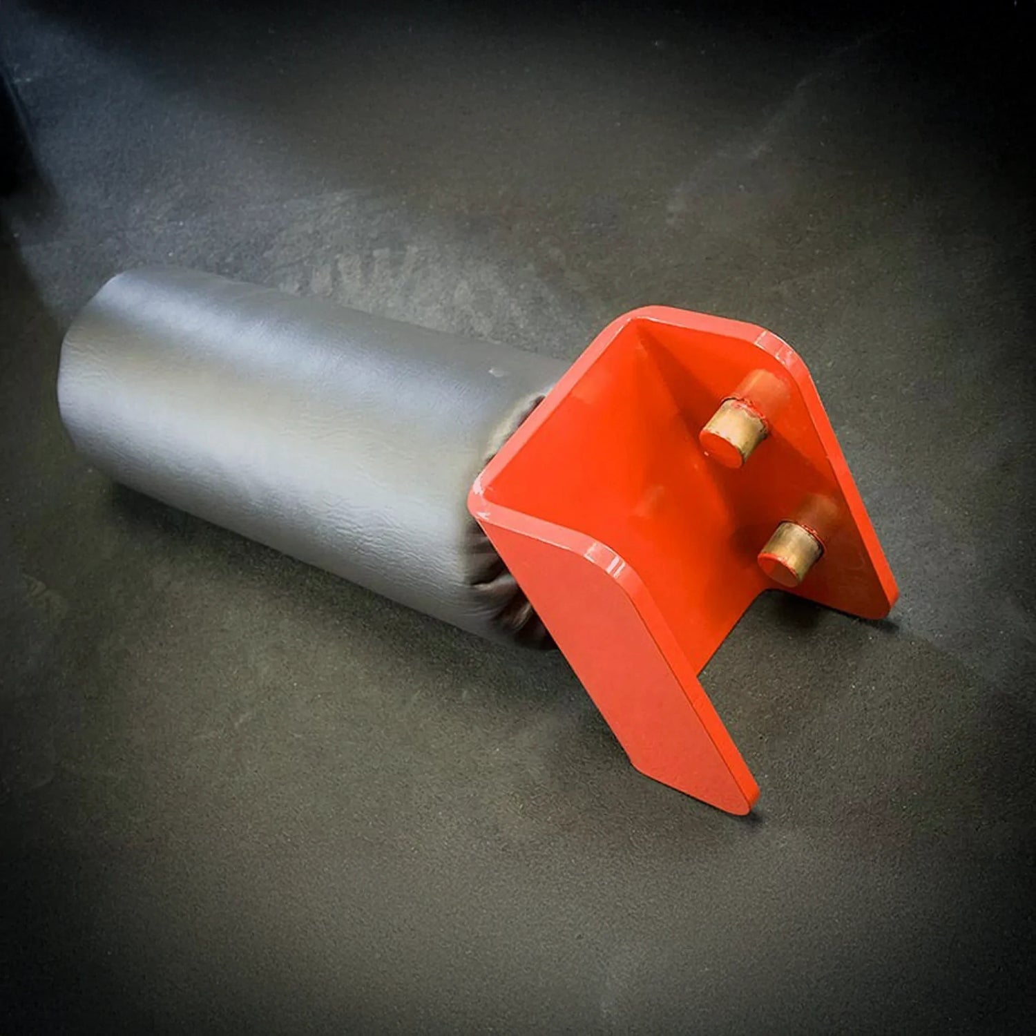 A black and red leg roller attachment sitting on a black rubber floor