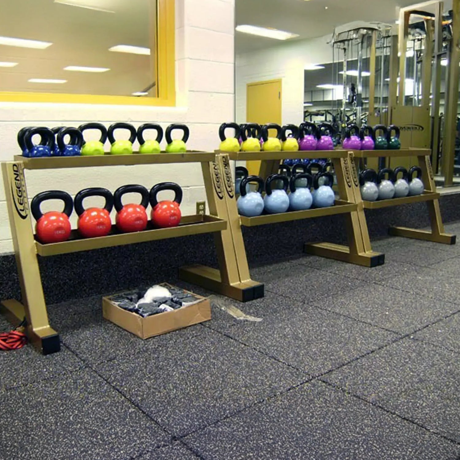 Three gold kettlebell racks with colorful kettlebells in a gym setting
