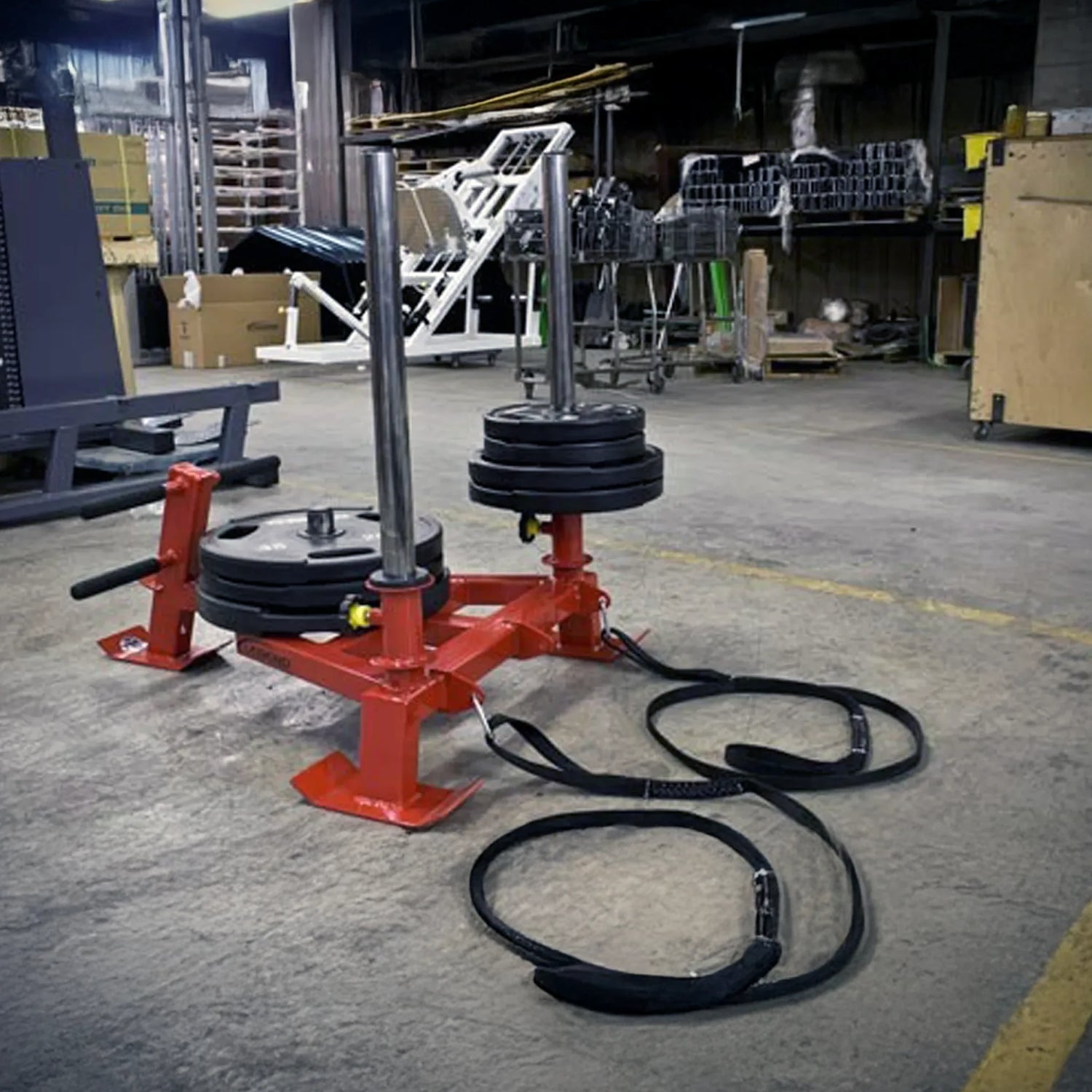 A red fitness sled with black weight plates on it in a warehouse setting