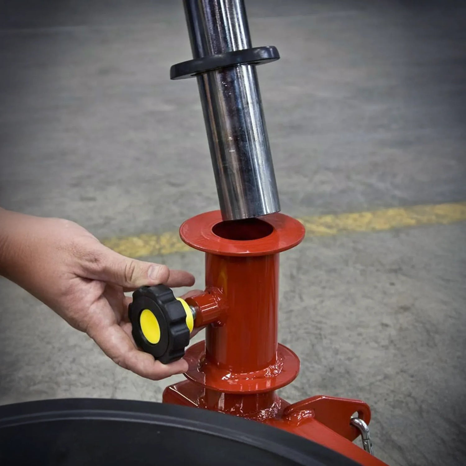 Hand adjusting a yellow and black knob on red mechanical equipment on a gray concrete surface