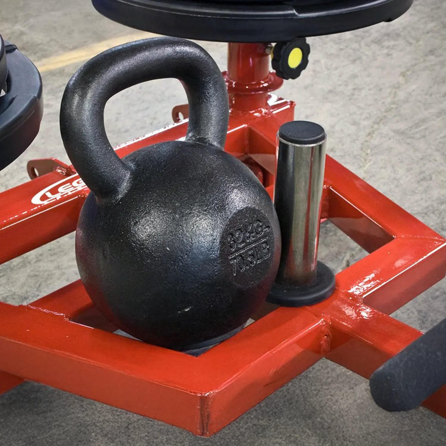 A black kettlebell on red metal equipment on a gray concrete floor