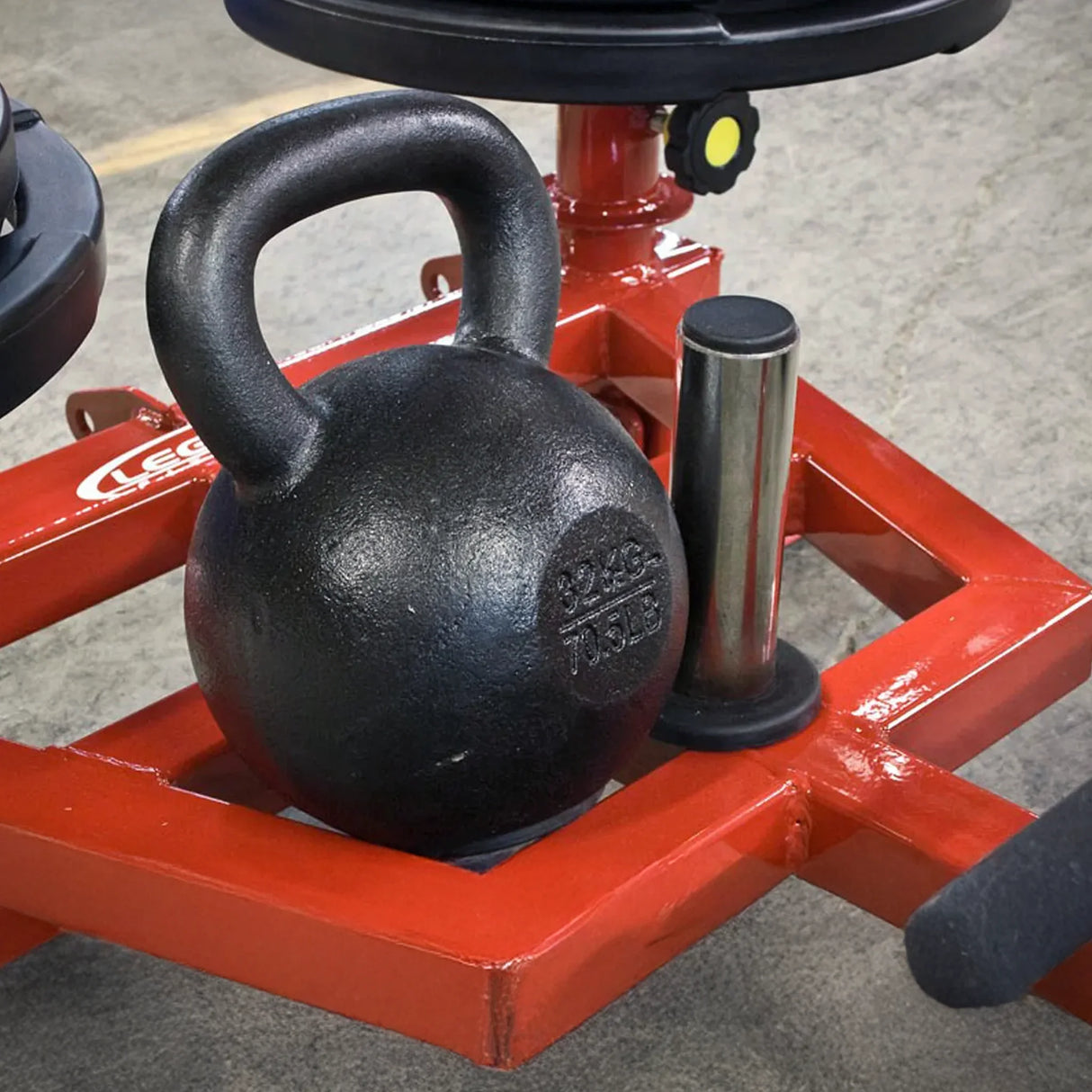 A black kettlebell on red metal equipment on a gray concrete floor