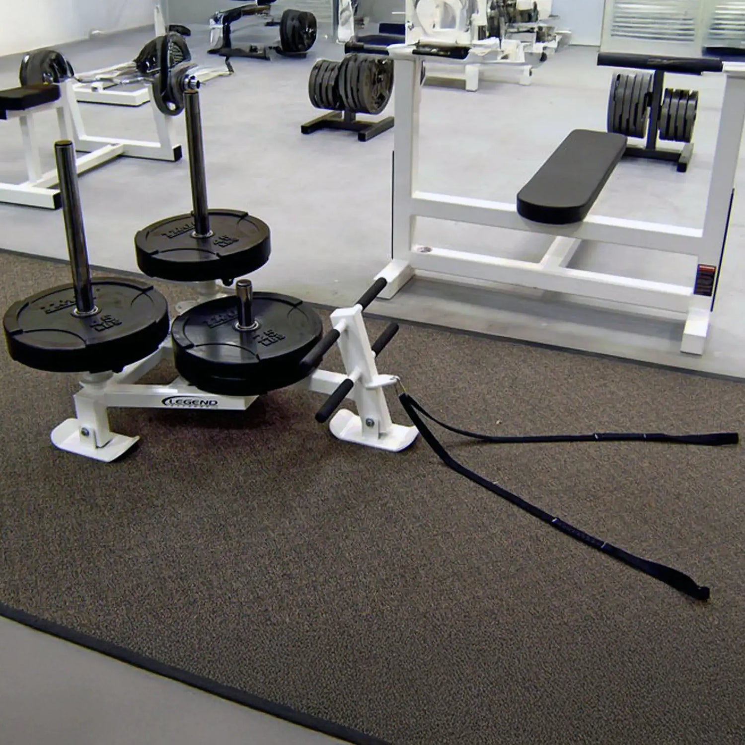 A white fitness sled with black weight plates on it in a gym setting