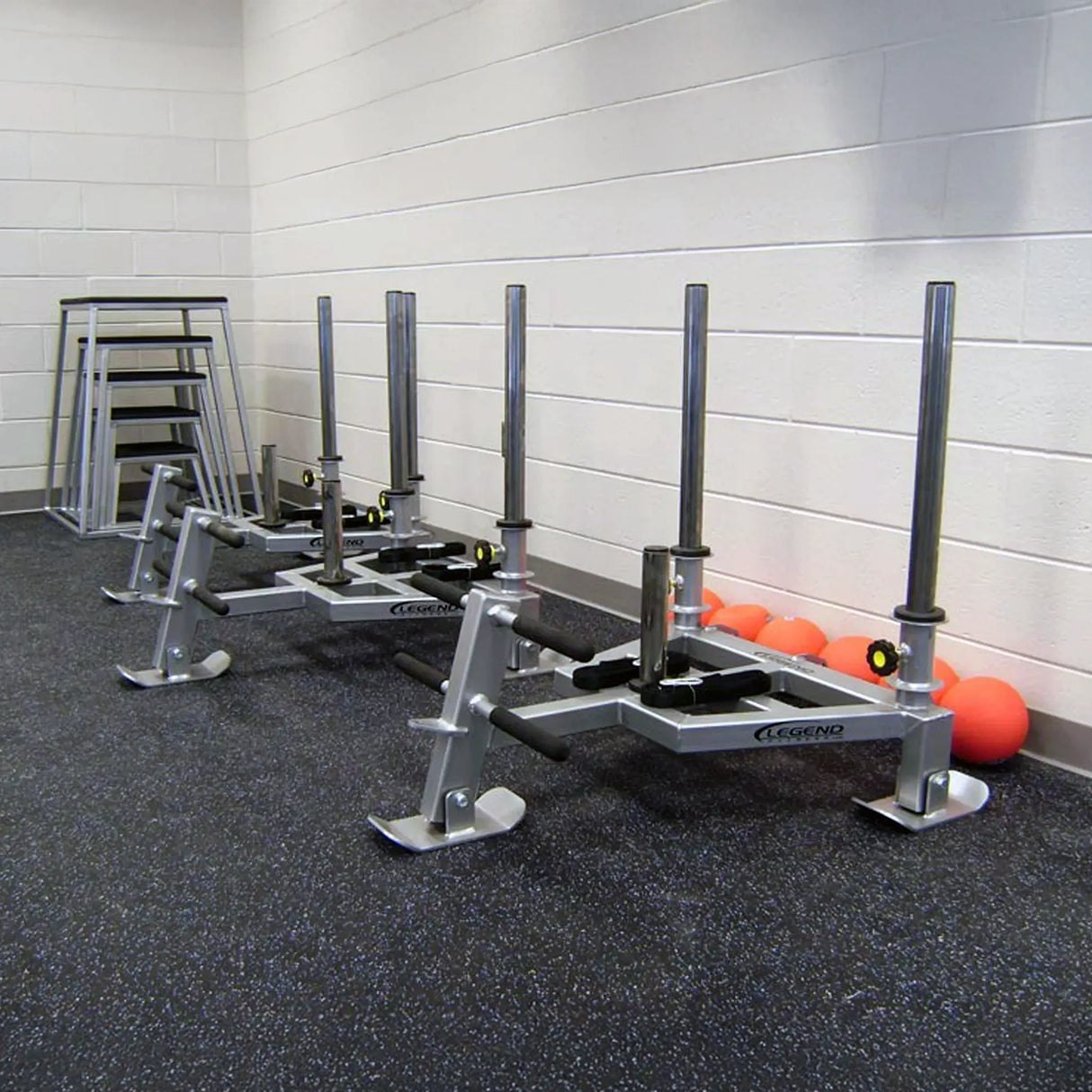Three gray fitness sleds against a white wall in a gym setting