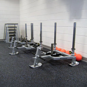Three gray fitness sleds against a white wall in a gym setting