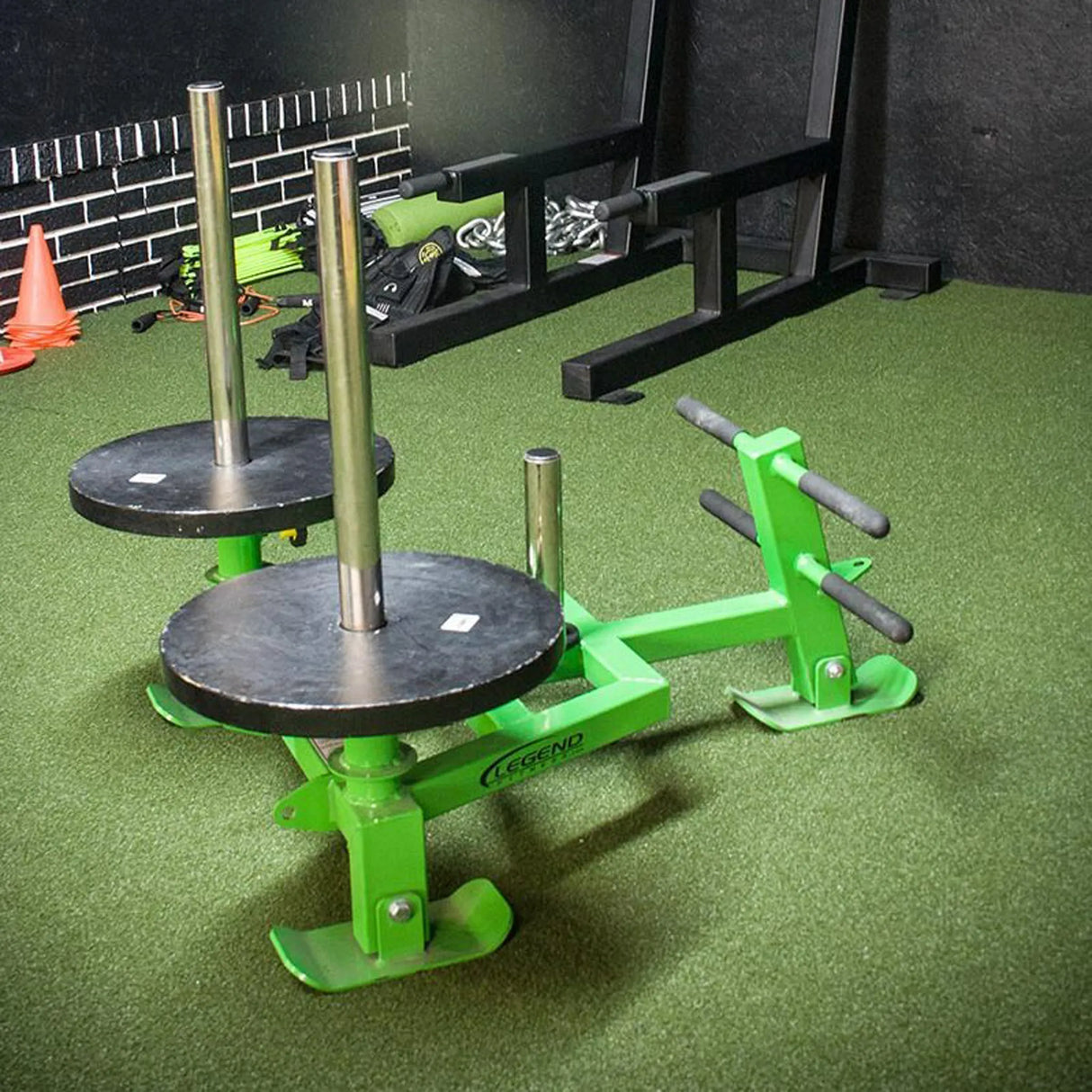 A green fitness sled with black weight plates on it in a gym setting