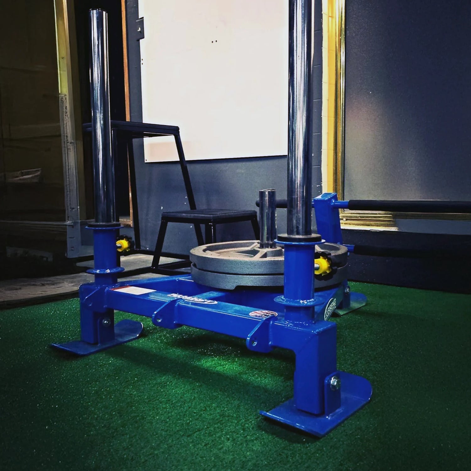 A blue fitness sled with gray weight plates on it in a gym setting