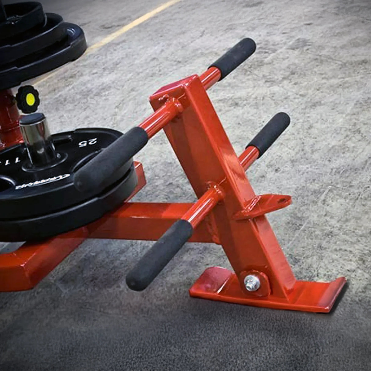Red metal equipment with black weight plates on it on a concrete floor