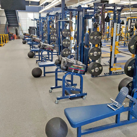 Gym equipment including weight plates and benches in a well-lit indoor setting.