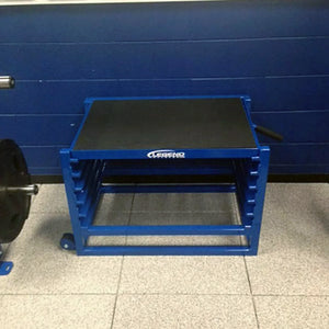 A blue metal adjustable step up box against a blue wall on a white floor in a gym setting