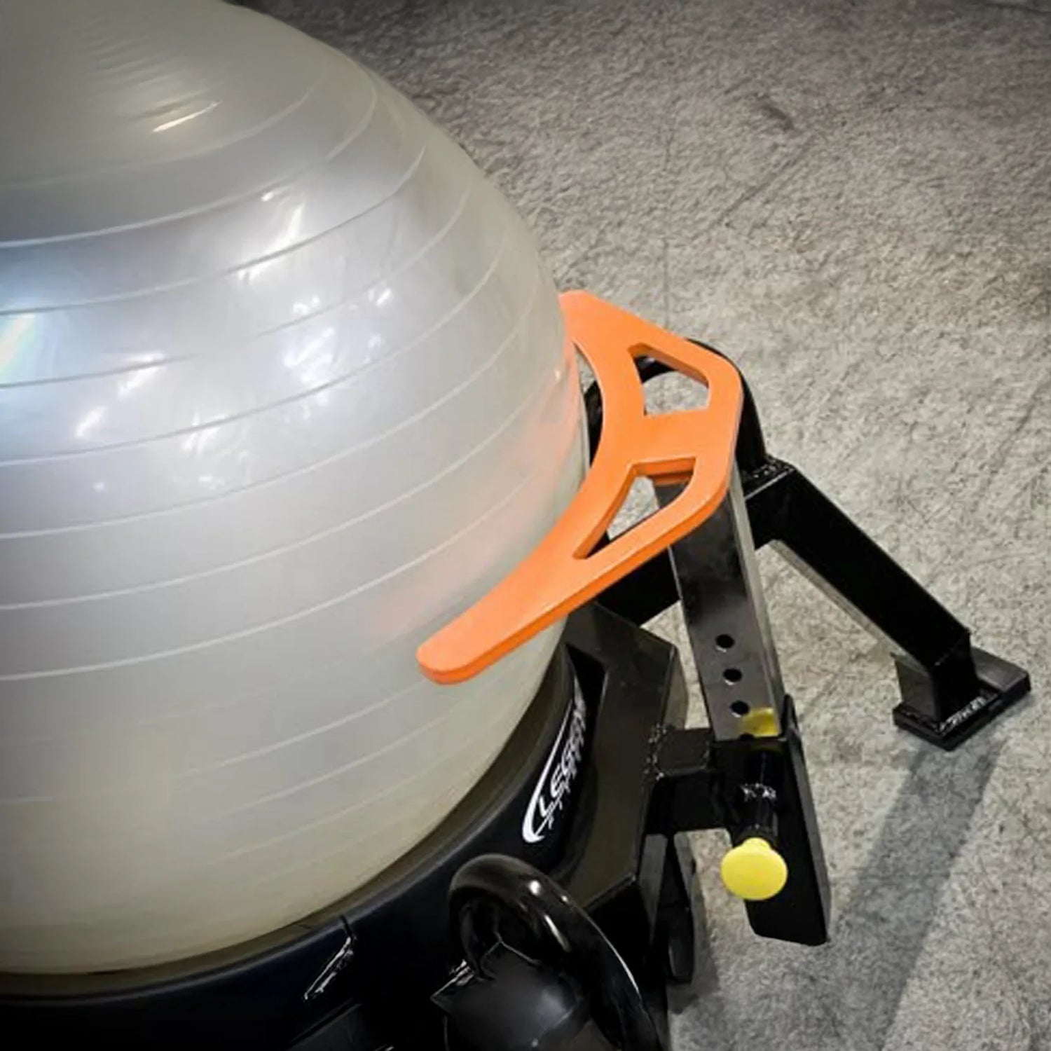 A white exercise ball on a piece of fitness equipment on a concrete floor