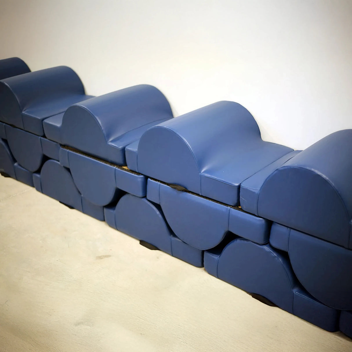 A stack of blue upholstered fitness pads up against the white wall