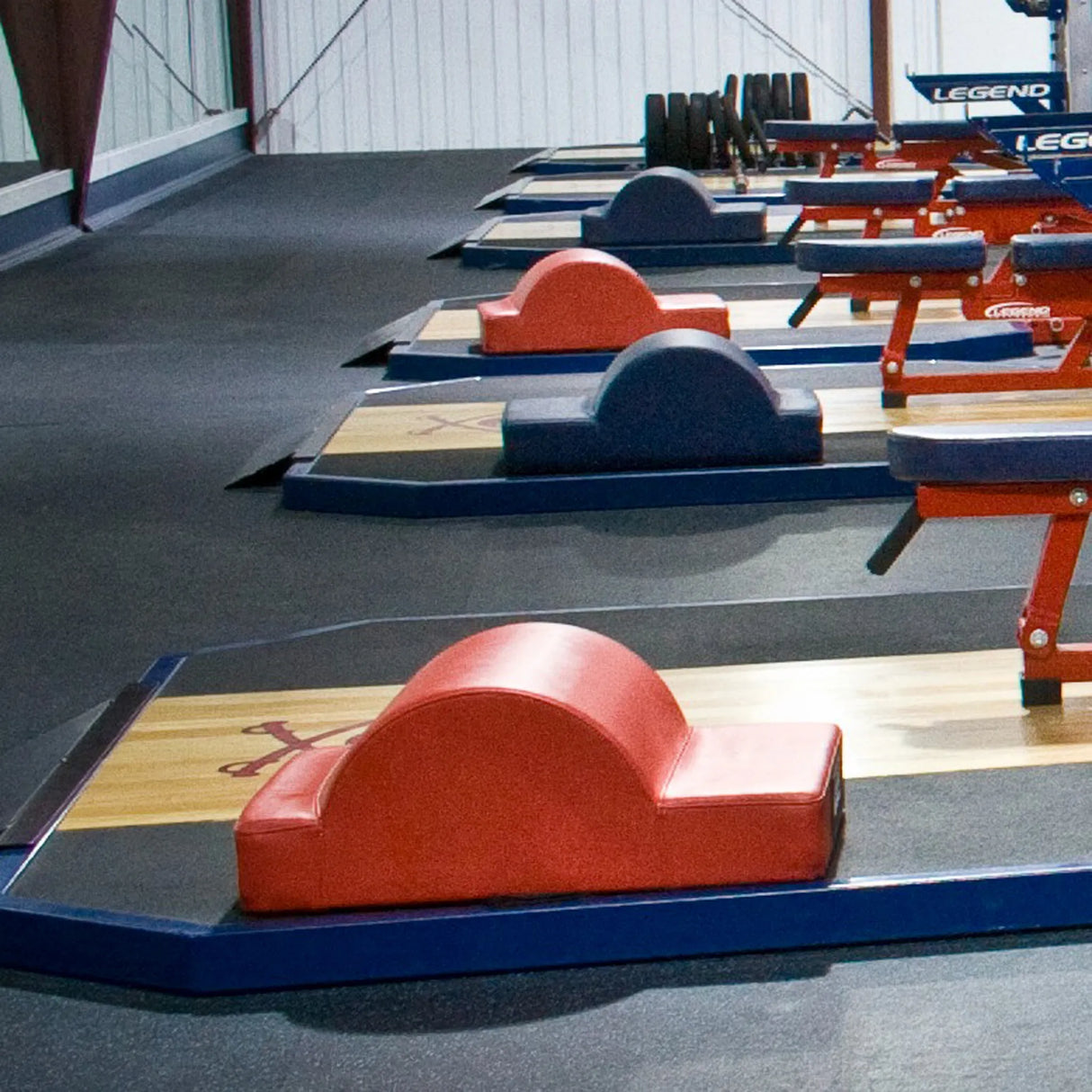 A row of wooden and rubber lifting platforms with glute ham developer fitness pads on them in a gym setting