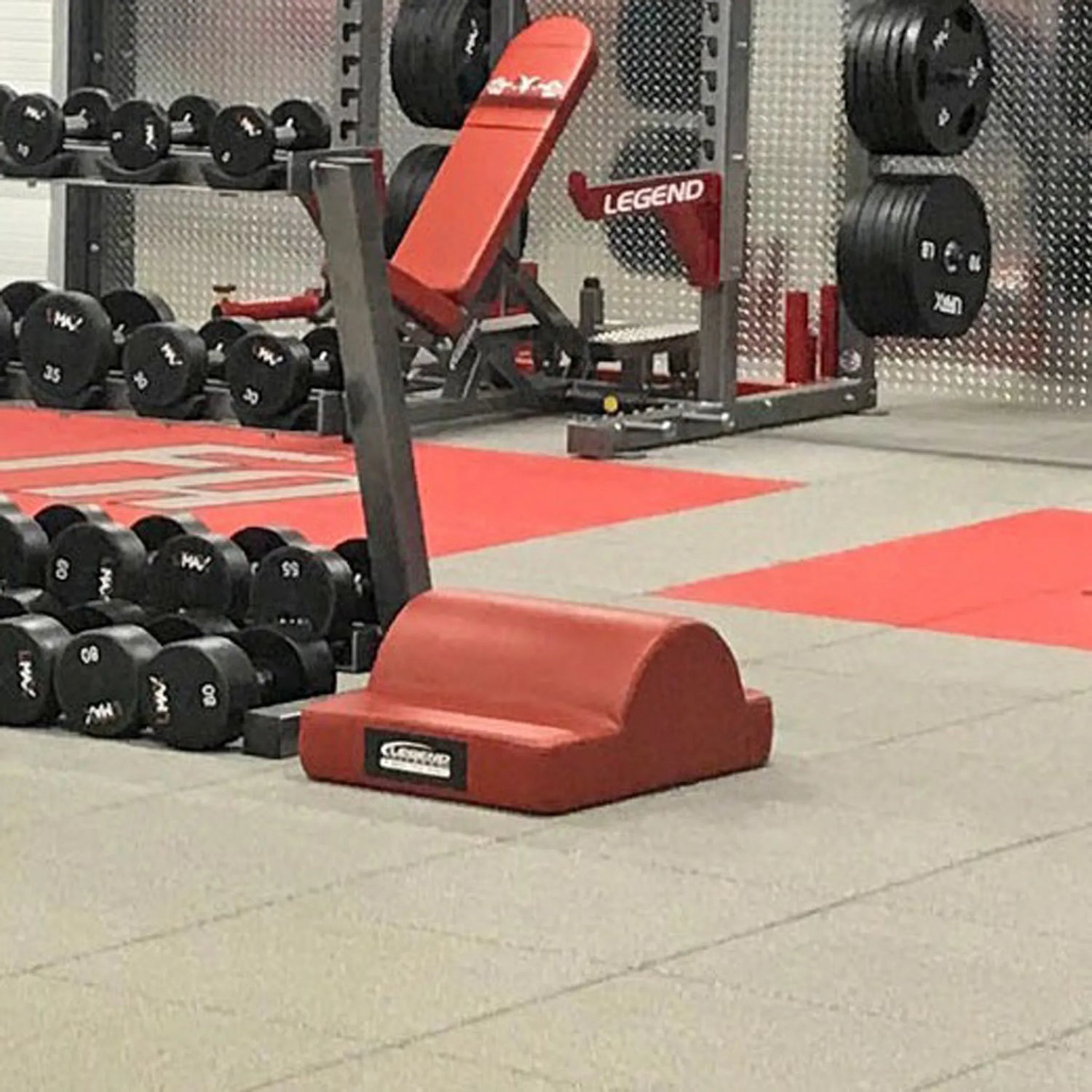 Gym equipment including weights and a red fitness pad on a tiled floor.